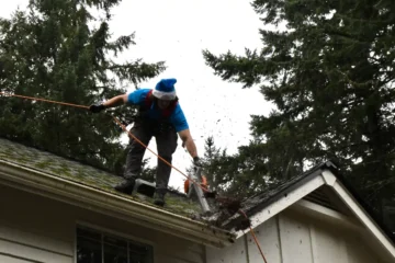 Johnny Tsunami technician clearing gutters and removing debris from a mossy PNW roof